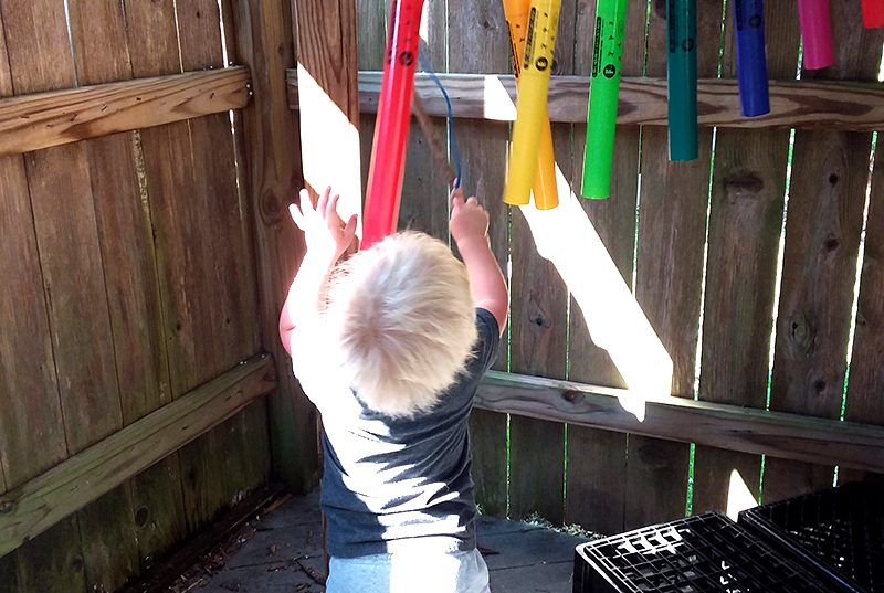 A toddler at Sugar Mill Montessori School playing with colored tubes outside